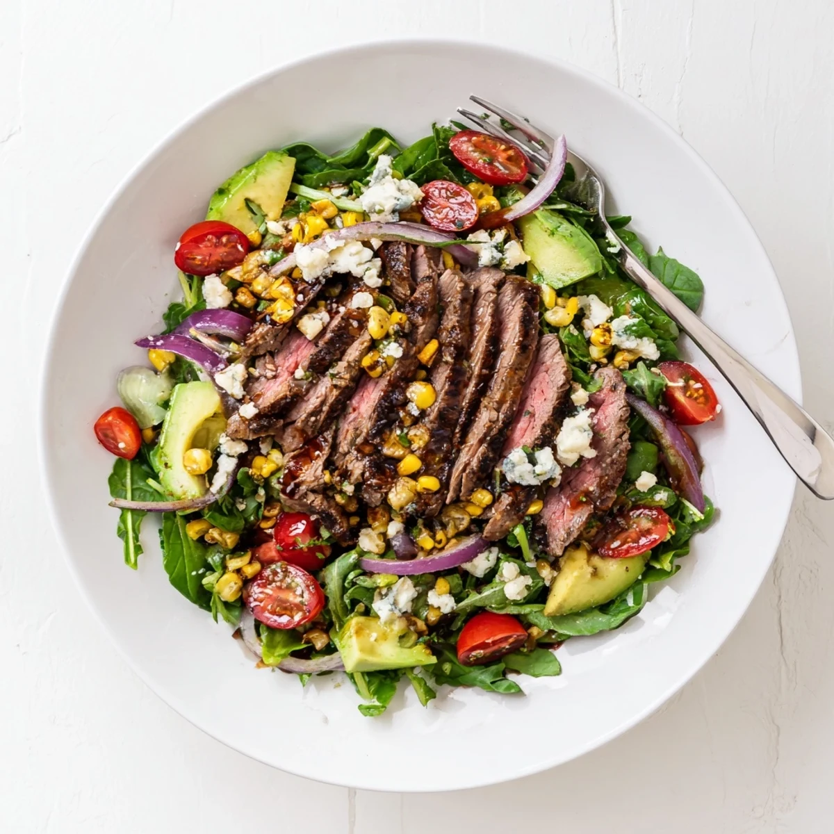 Sliced balsamic steak arranged over a colorful balsamic steak gorgonzola salad with grilled corn