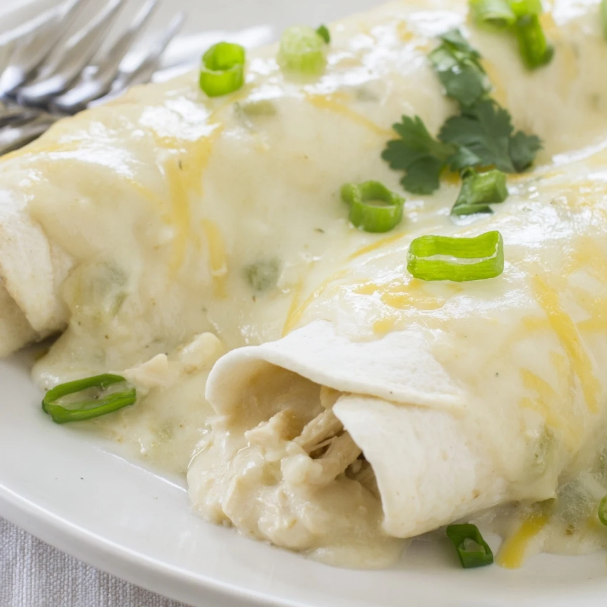 Creamy White Chicken Enchiladas bubbling with melted cheese, golden edges, cilantro garnish