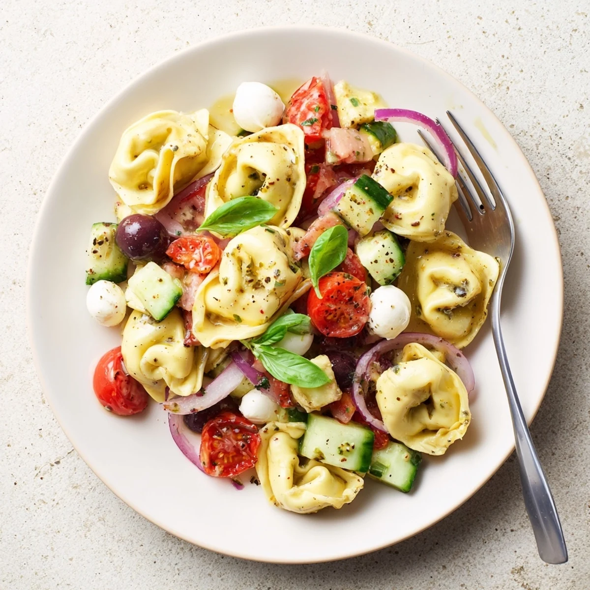Forkful of Tortellini Pasta Salad showing mozzarella, cucumbers, olives, and herbs