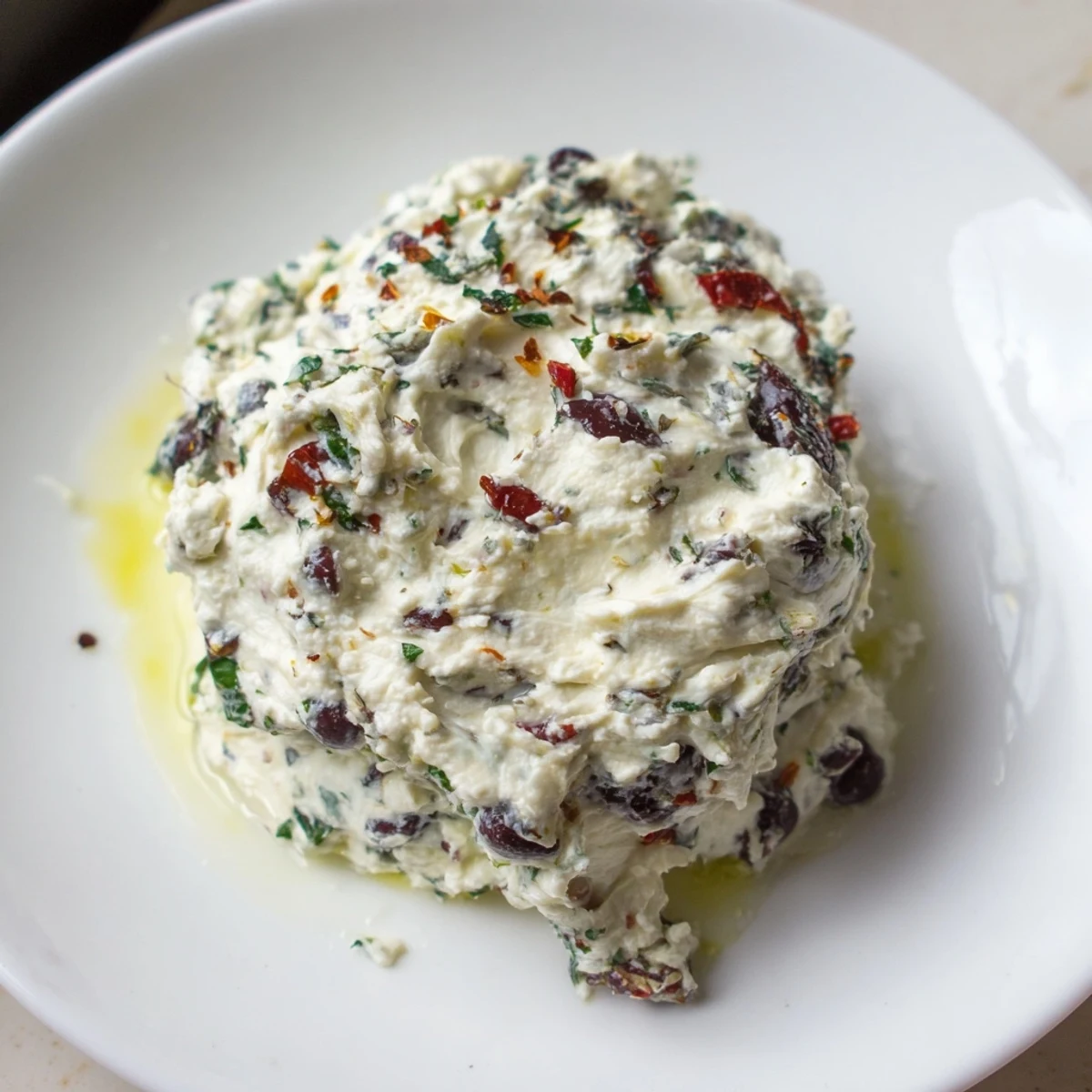 A rustic bowl of Italian Style Olive and Cheese Spread with green and black olives scattered on a wooden board