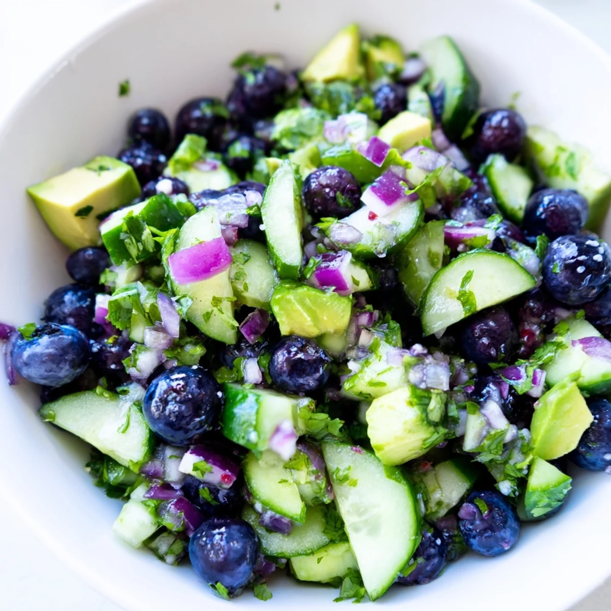 A close-up of blueberry cucumber salsa in a white bowl with tortilla chips nearby
