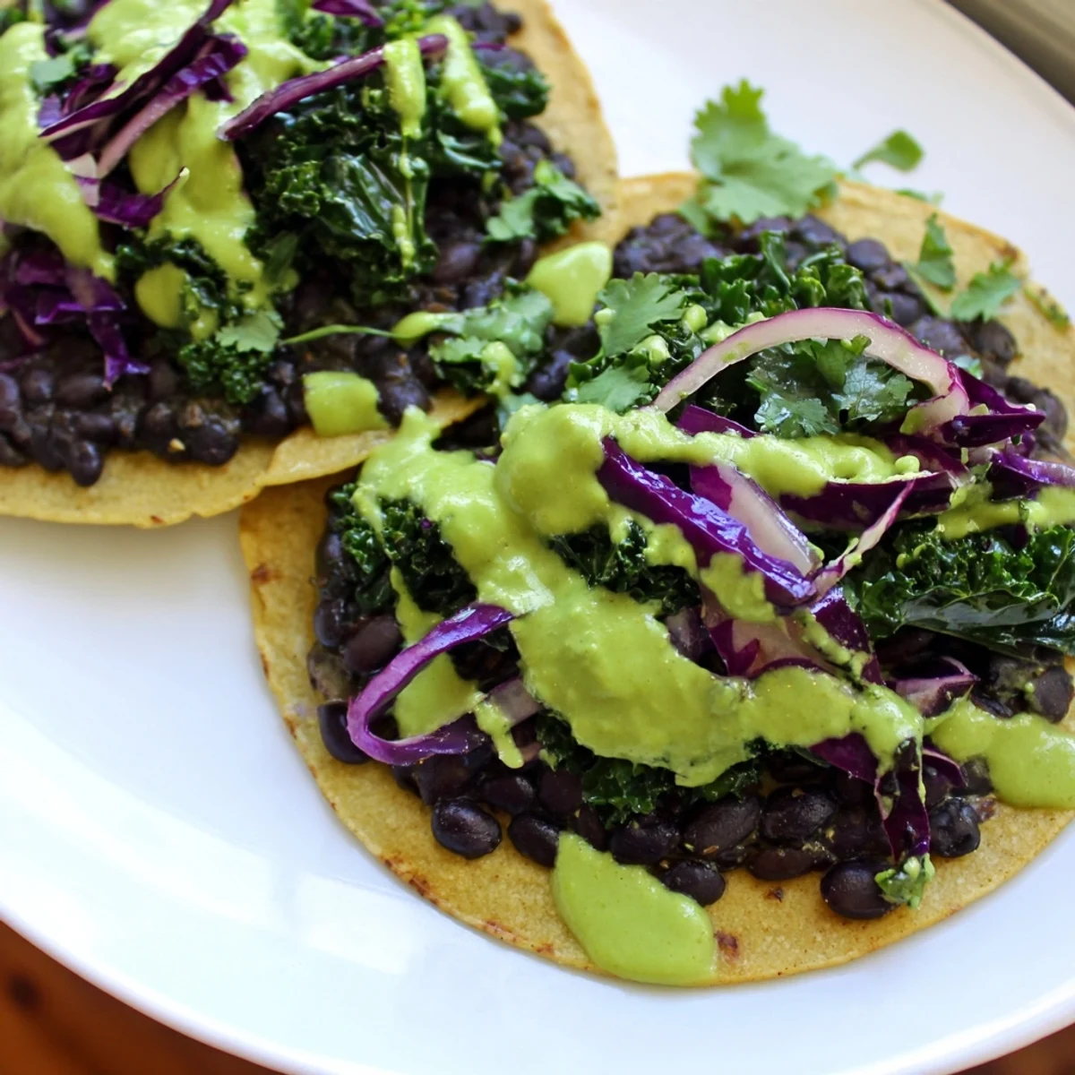 Warm Smoky Black Bean Kale Tacos drizzled with creamy green sauce on corn tortillas