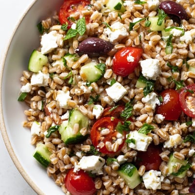Close-up shot of Mediterranean Farro Salad, showing chopped herbs and Kalamata olives on fluffy grains.