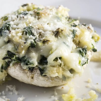 A close-up of Cheesy Spinach and Artichoke Stuffed Mushrooms with bubbling, golden-brown cheese topping and herbs.
