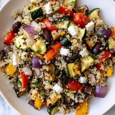 A wholesome Mediterranean Quinoa Salad topped with crumbled feta, kalamata olives, and fresh parsley sits on a rustic wooden table.