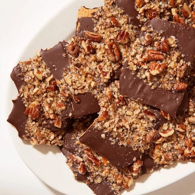 A close-up of chocolate covered matzo crackers with colorful sprinkles and shredded coconut, served alongside a steaming mug of coffee.  